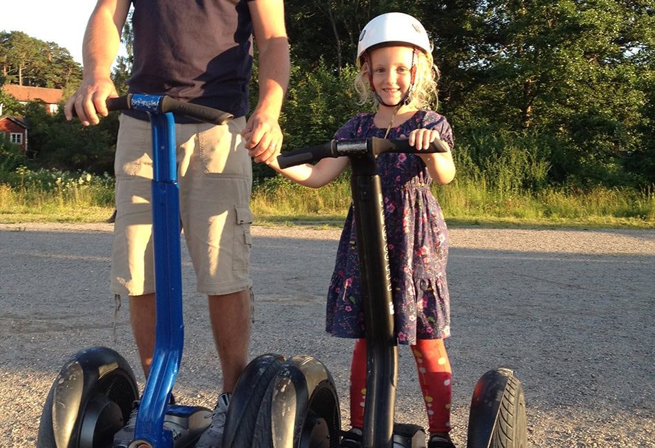 En liten flicka står på en Segway bredvid sin pappa.